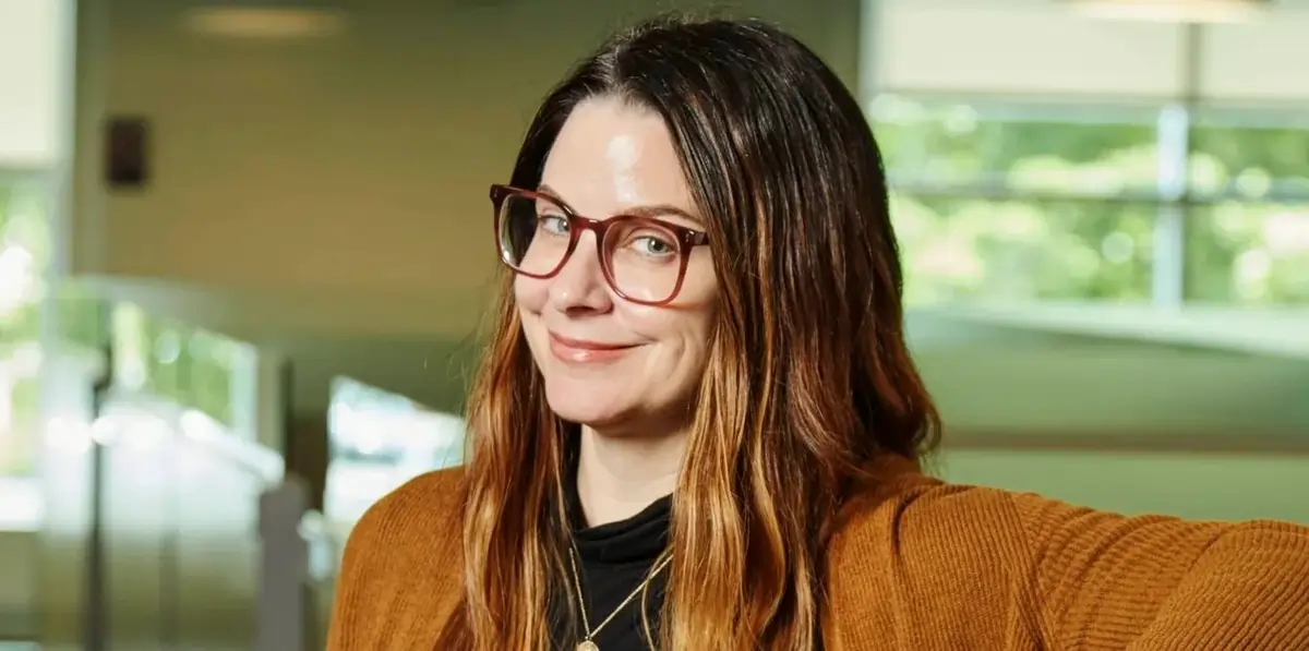 Jess Lanzillo sorri enquanto posa para uma foto em ambiente corporativo iluminado.